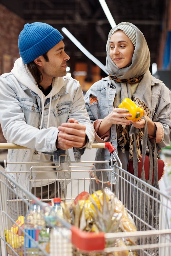 Happy couple shopping together in a supermarket with a full cart of groceries.